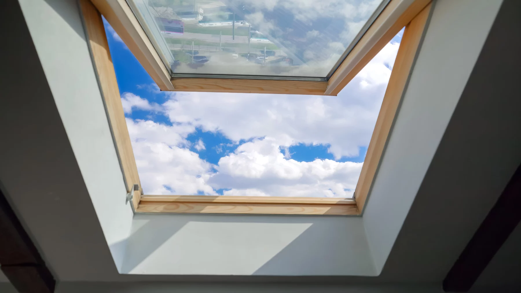 Blick durch ein Dachfenster auf blauen Himmel und Wolken